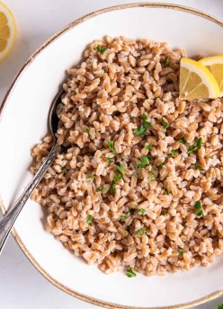 Cooked farro in a bowl with lemon and fresh herbs.