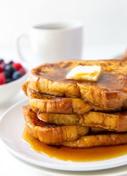 five slices of french toast stacked on a plate served with butter and maple syrup