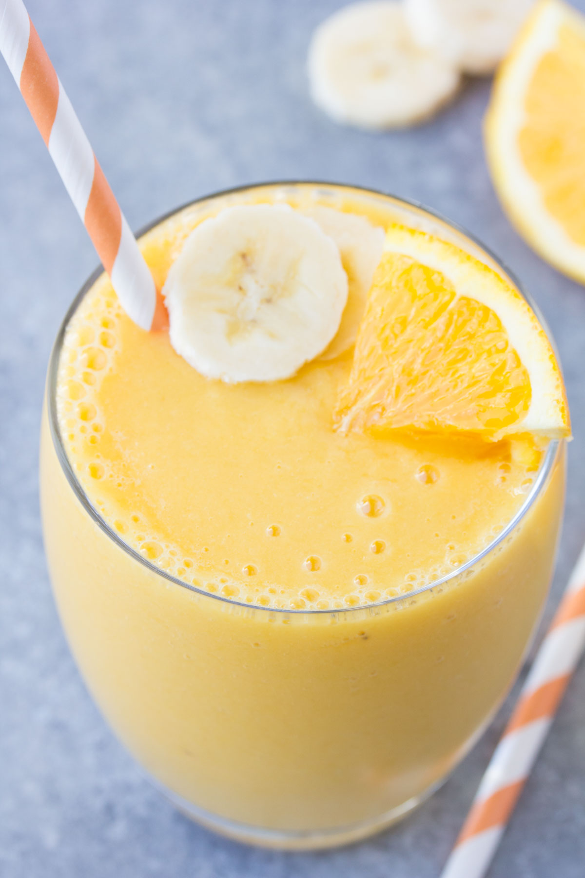 Orange smoothie in a glass with banana slice and orange wedge.