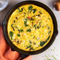 Baked frittata with spinach, bell pepper, mushrooms, onion and goat cheese in a cast iron skillet.