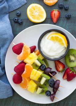 Rainbow fruit kabobs on a white plate with lemon Greek yogurt dip.