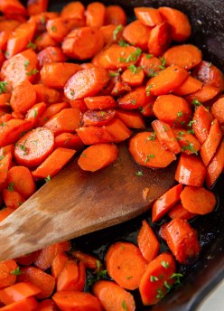 Close up of glazed carrots in skillet with wooden spoon.