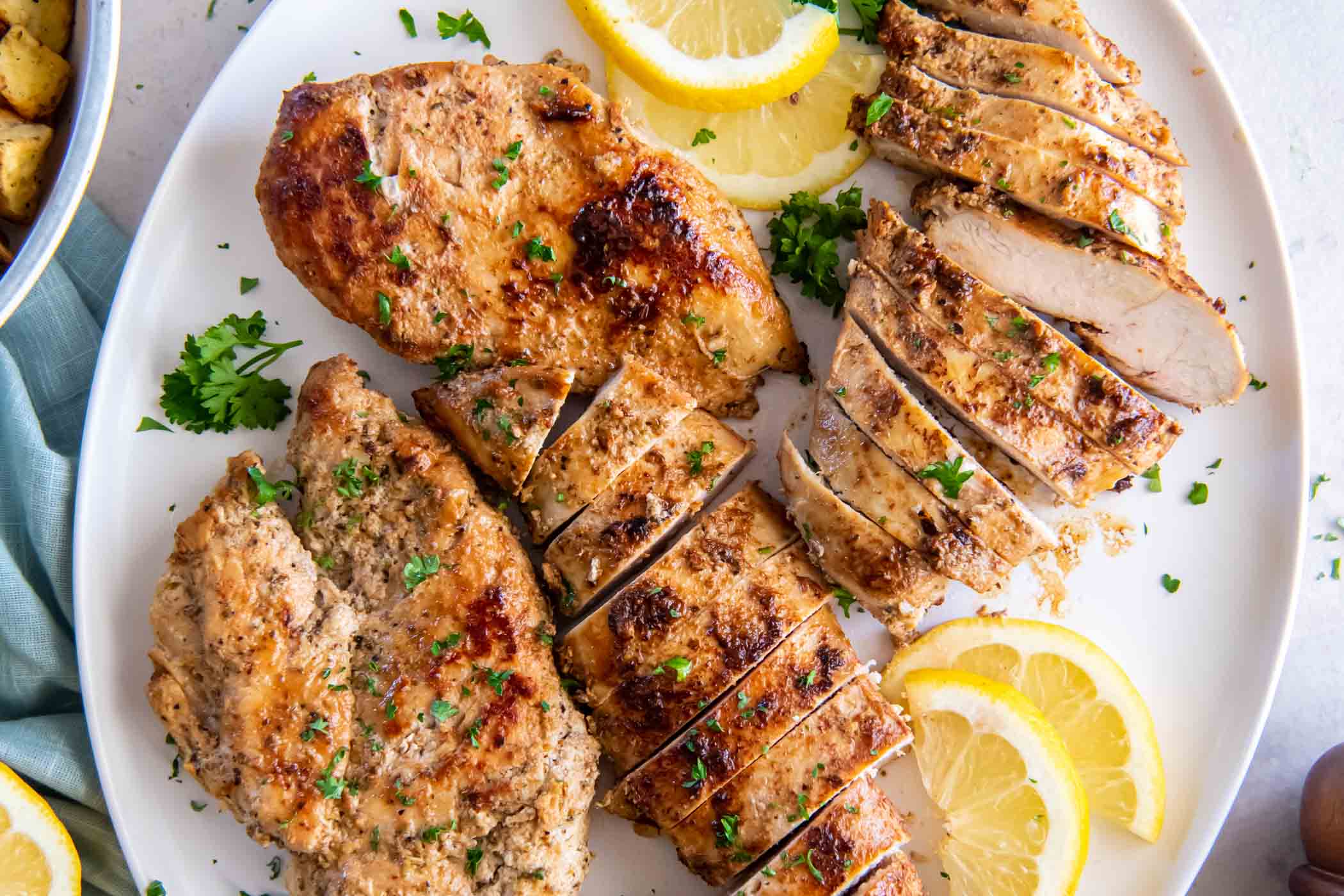 Four cooked Greek chicken breasts on a plate, partially sliced.