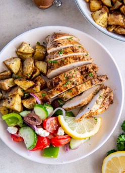 Sliced Greek chicken breast served with roasted potatoes and greek salad.