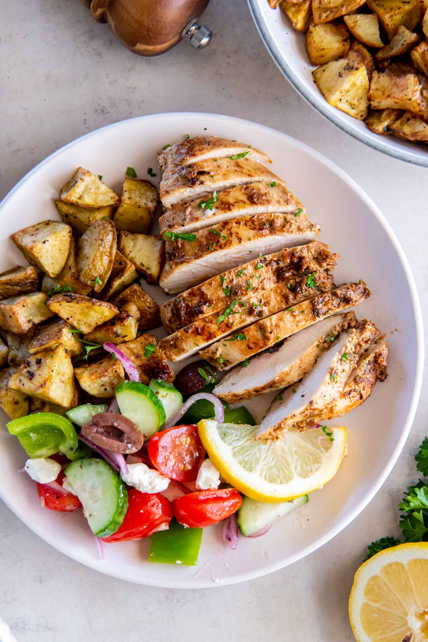 Sliced Greek chicken breast served with roasted potatoes and greek salad.