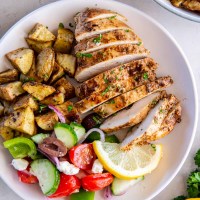 Sliced Greek chicken breast served with roasted potatoes and greek salad.