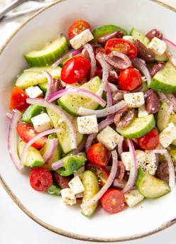 close up of greek salad tossed with dressing in a bowl