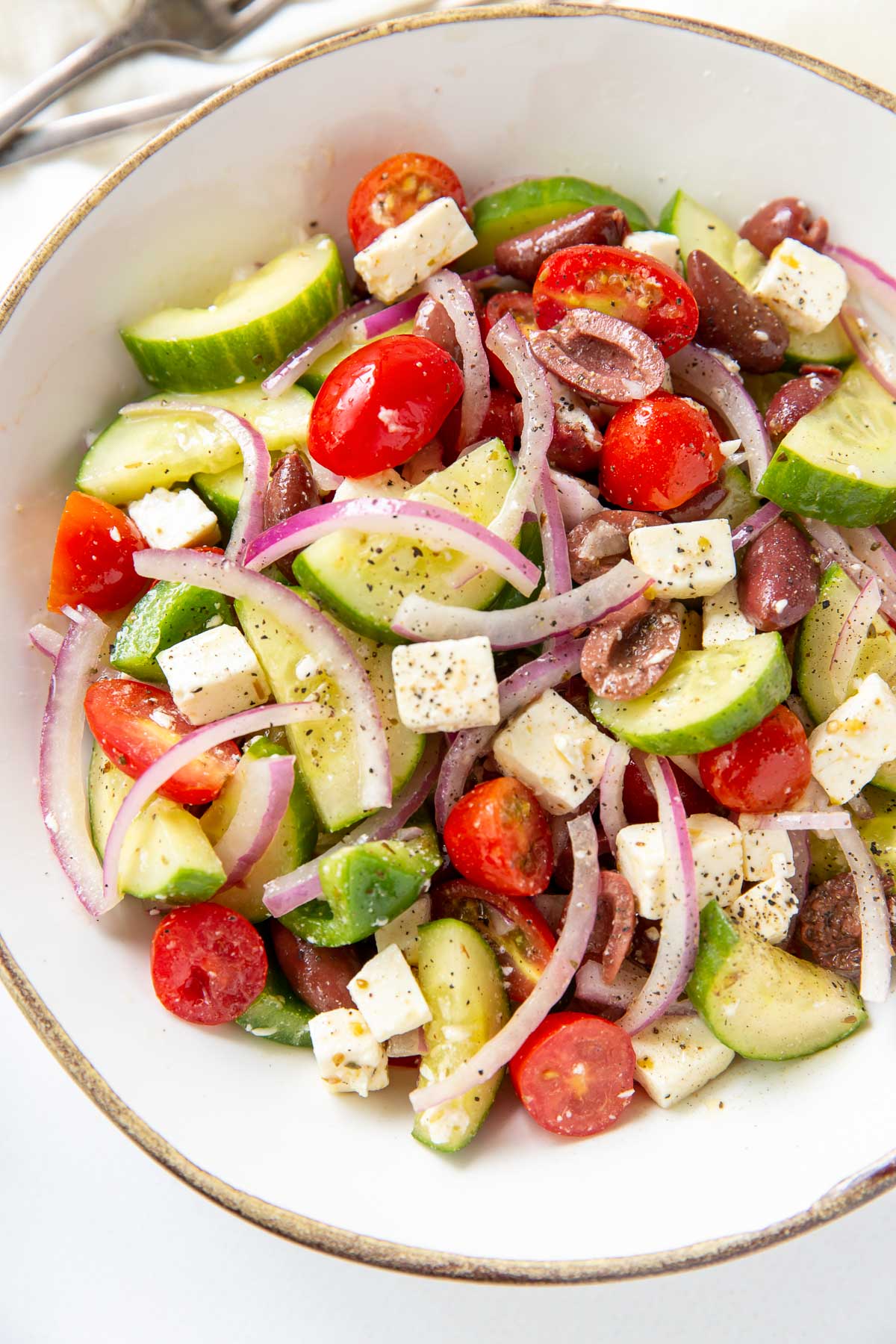 Close up of greek salad tossed with dressing in a bowl.