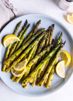 Grilled asparagus served on a light blue plate with lemon wedges.