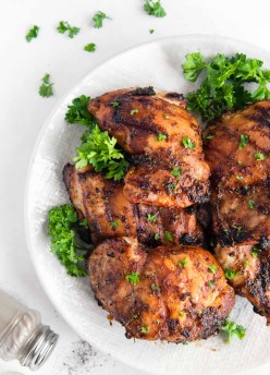 grilled boneless chicken thighs stacked on a plate with parsley garnish