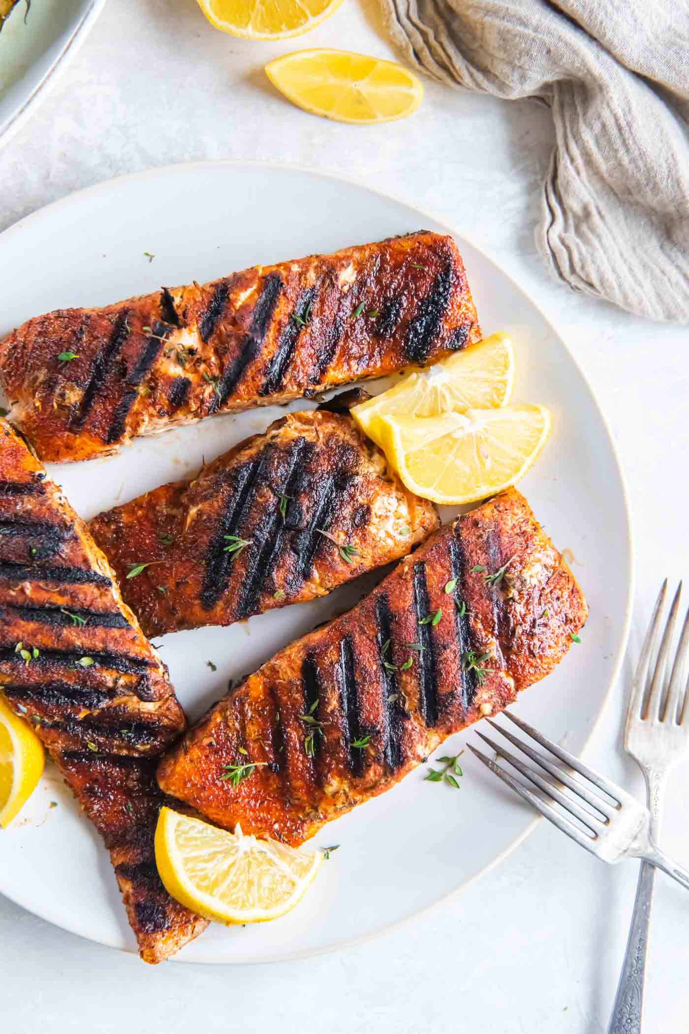 Four grilled salmon fillets on a plate with lemon wedges.
