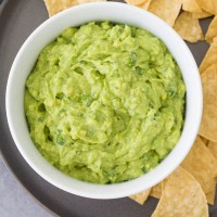 Guacamole served in a white bowl with tortilla chips.