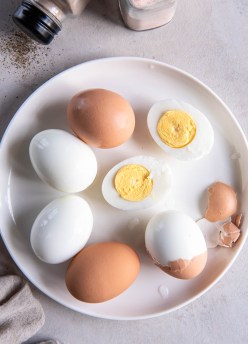 Hard boiled eggs on a plate with some unpeeled, some peeled and some cut in half.
