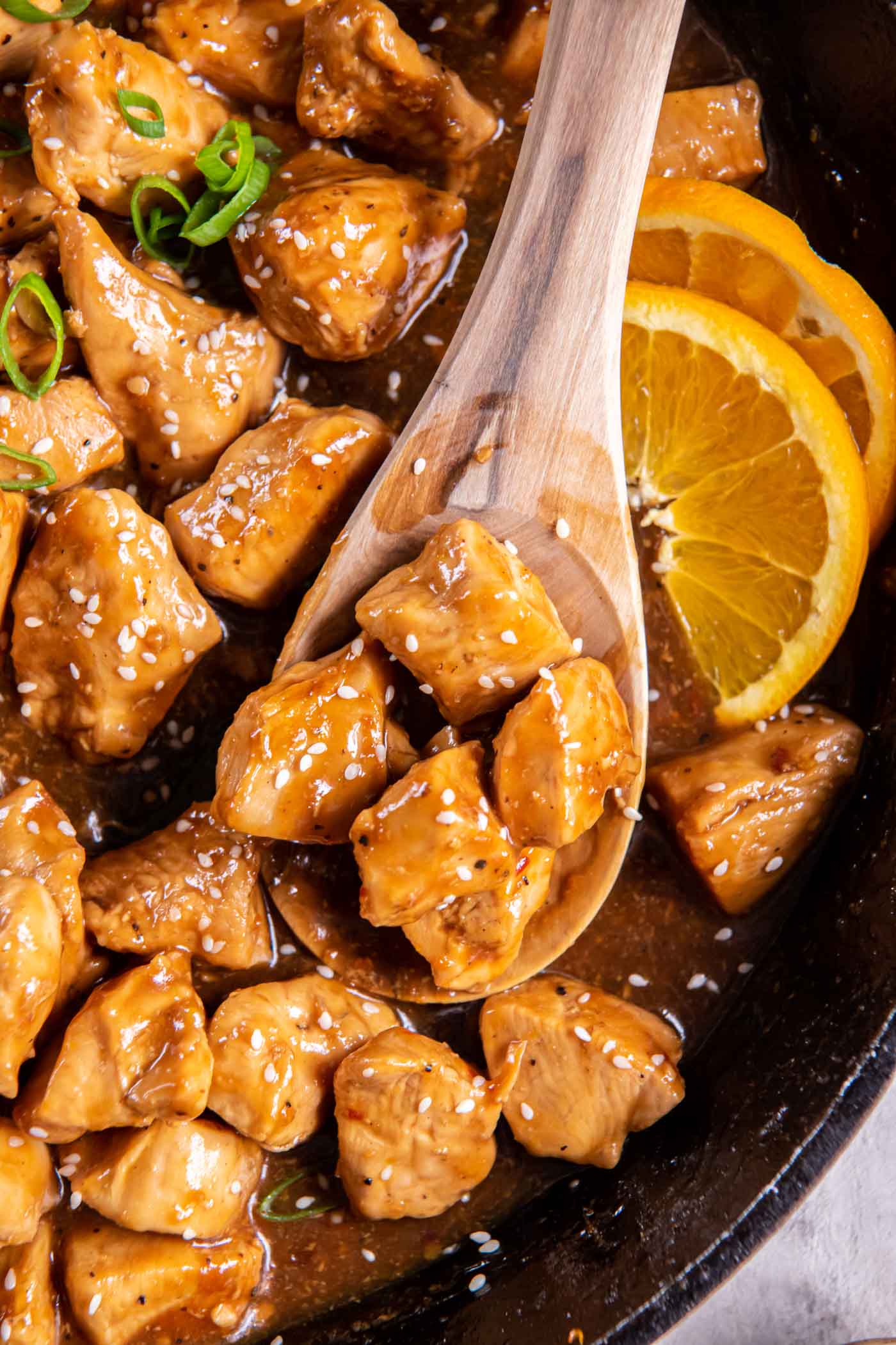Close up of orange chicken on a wooden spoon set in skillet.