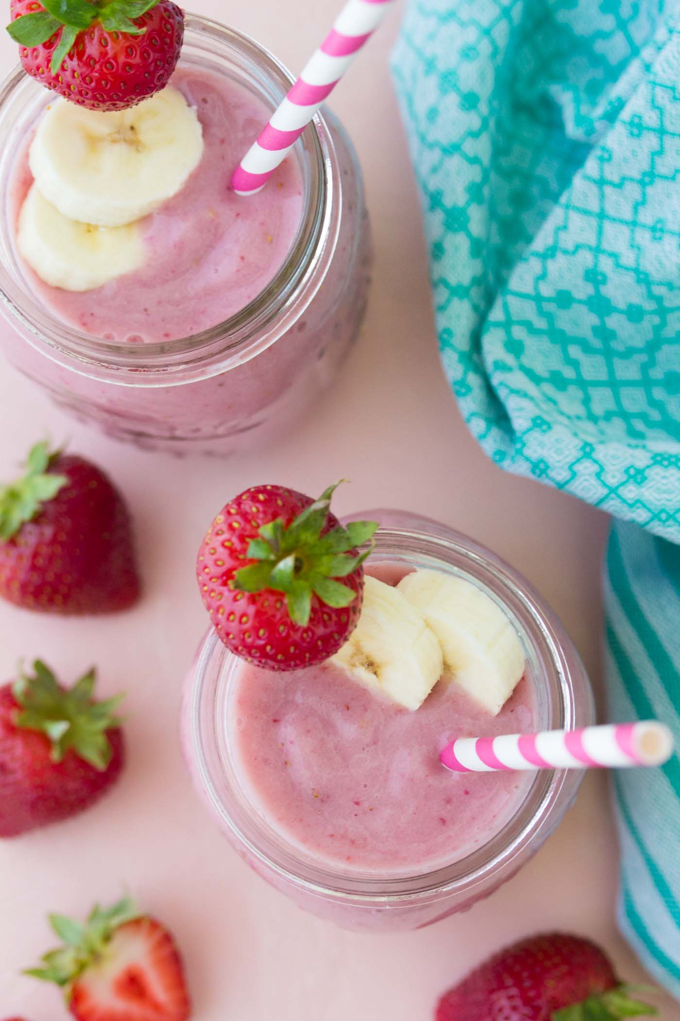 Two strawberry banana smoothies in mason jars with straws.
