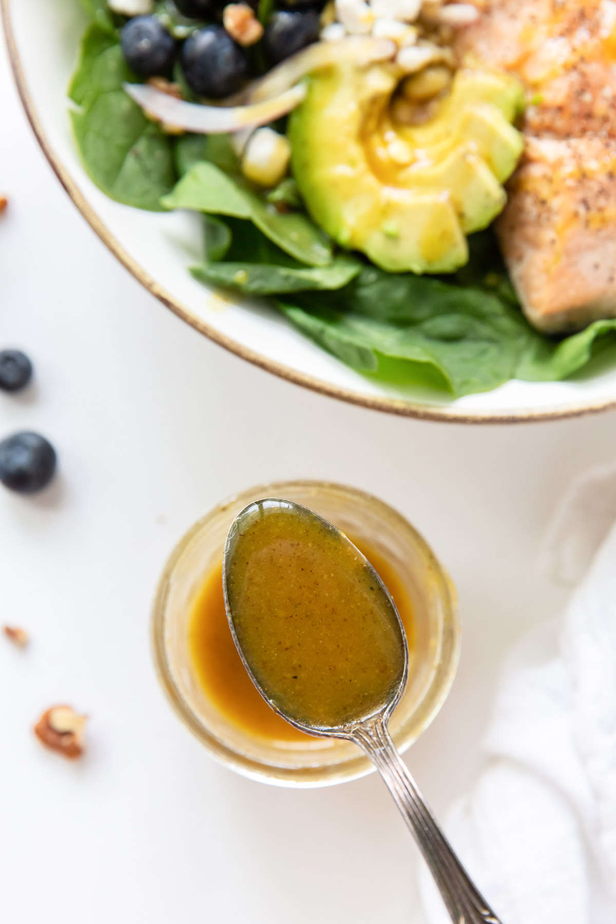 Homemade honey mustard dressing on a spoon held over a small jar with a salad in the background.