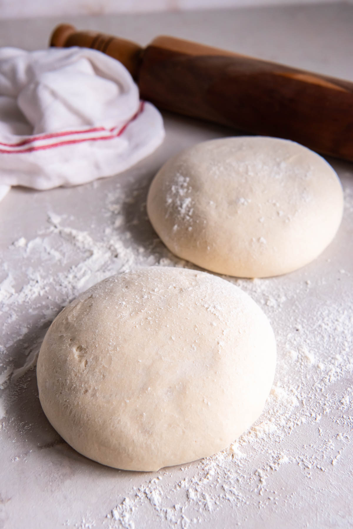 Two balls of pizza dough after rising on floured work surface.