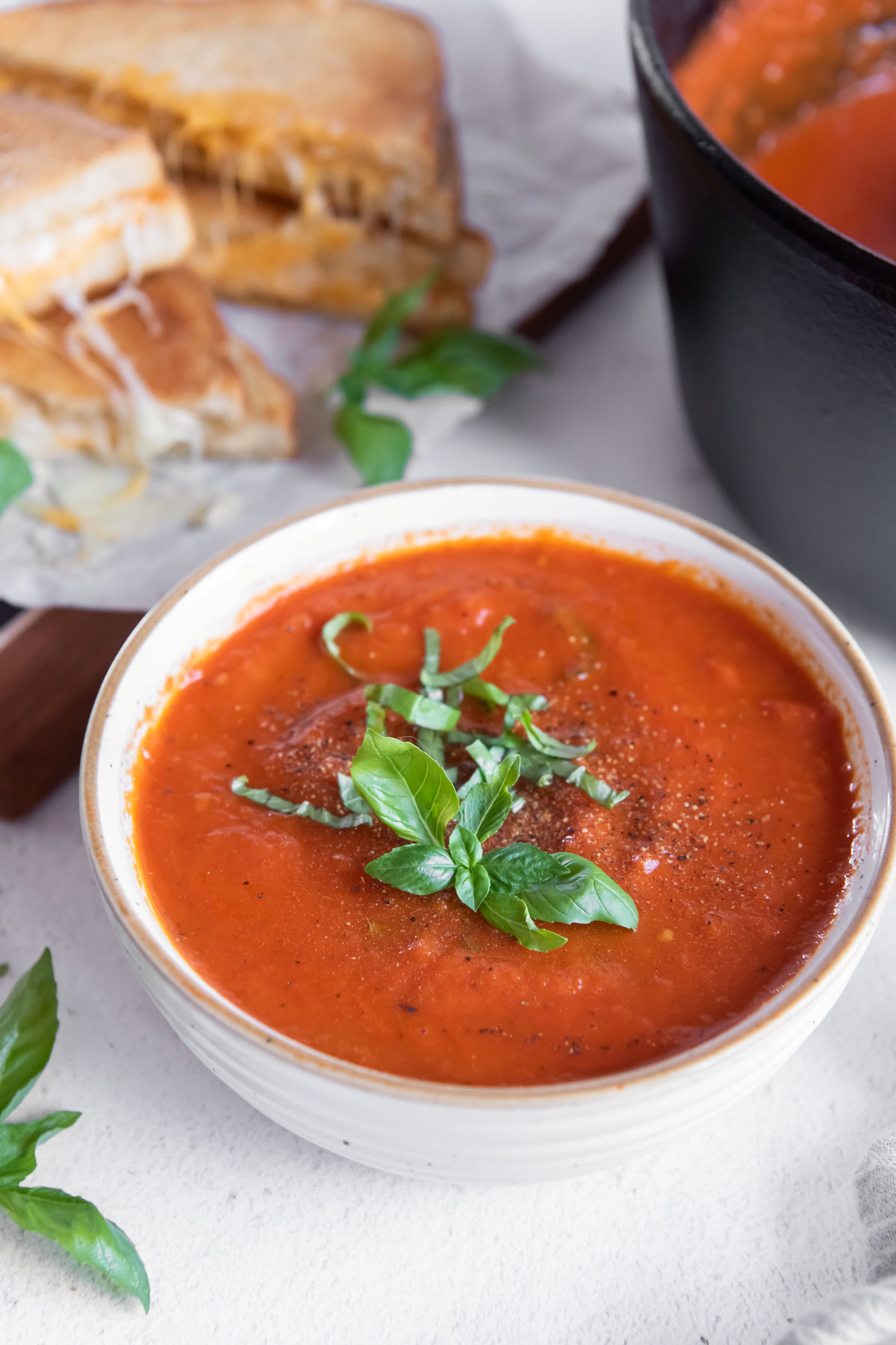 bowl of homemade tomato soup with grilled cheese in background
