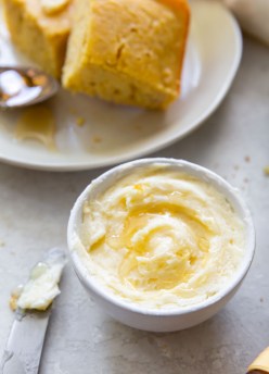 honey butter in a small white bowl with a butter knife next to and cornbread in background