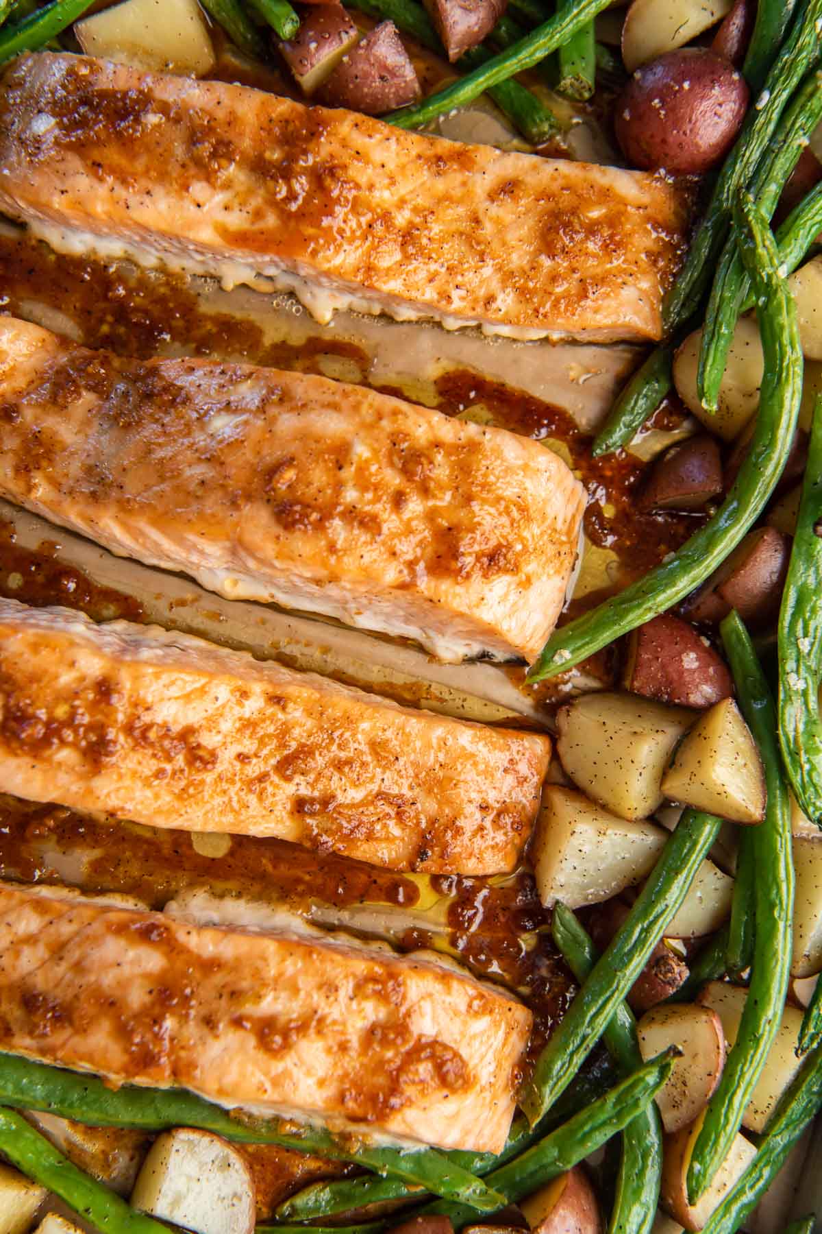 Honey garlic salmon with potatoes and green beans on baking sheet.