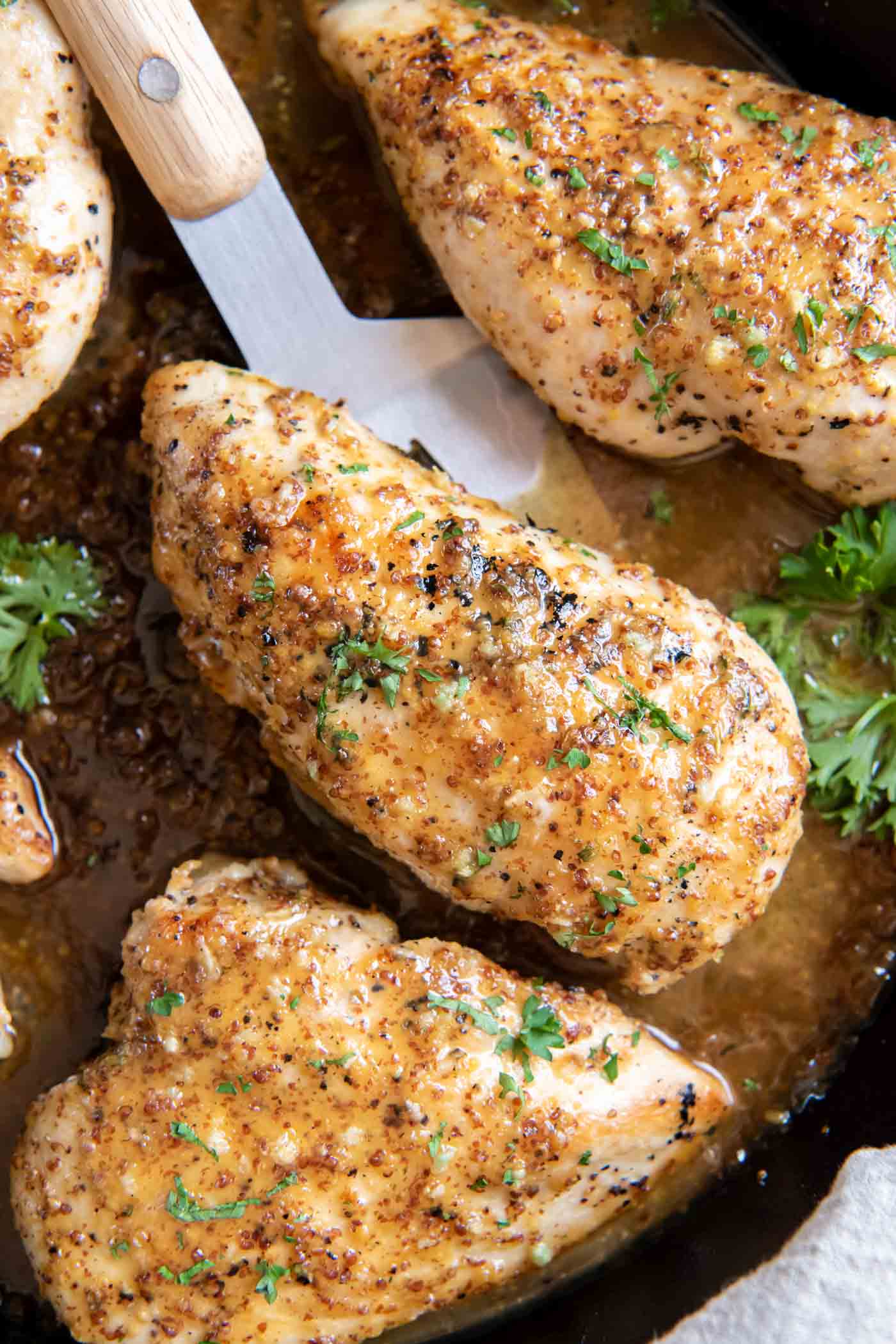 Honey mustard chicken breasts in a skillet with a serving spatula.