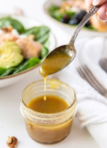 Homemade honey mustard dressing dripping off of a spoon into a small jar.