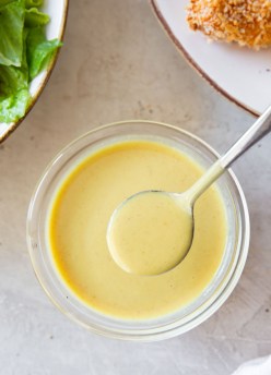 honey mustard on a spoon held over a glass dish