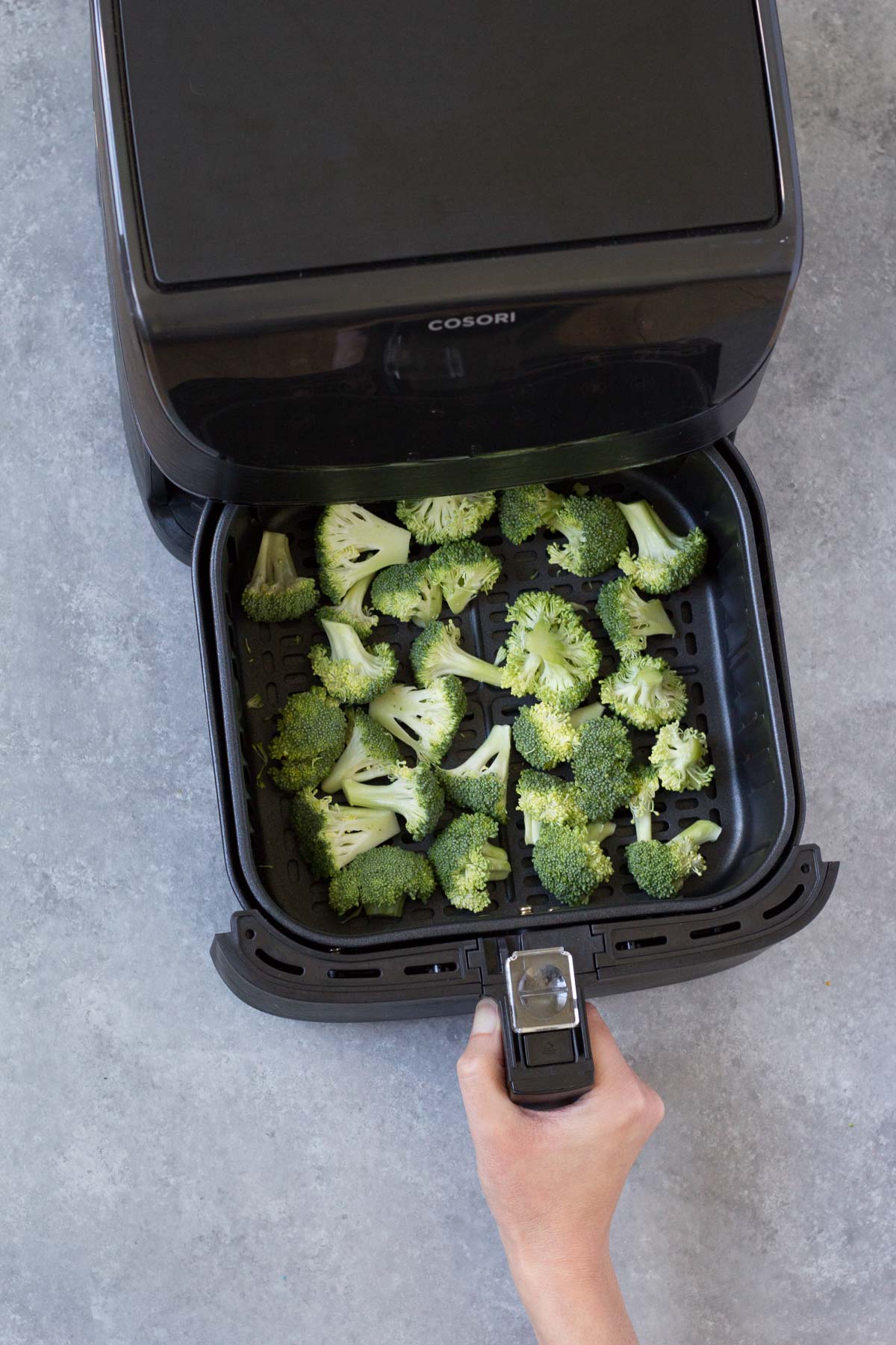 pulling out air fryer basket with broccoli in it
