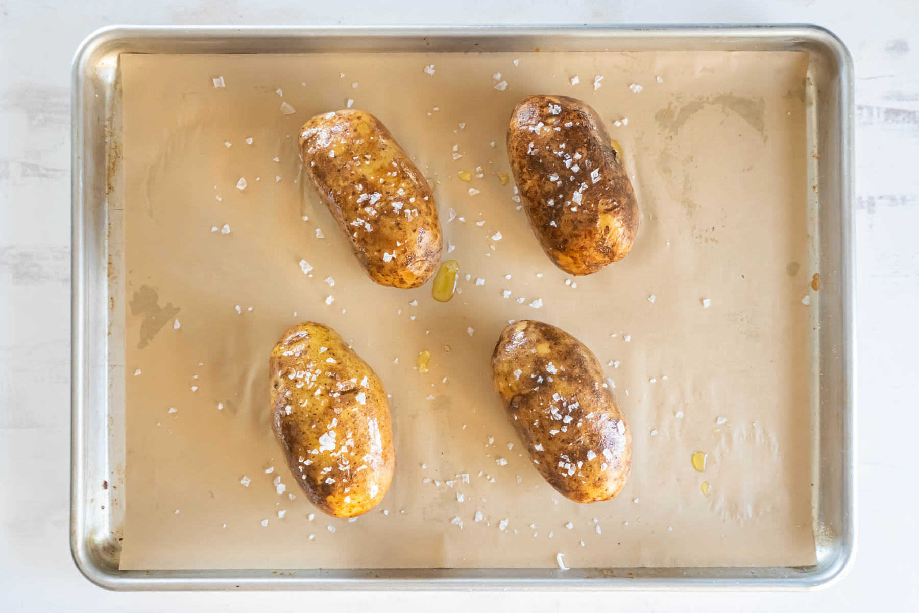 uncooked potatoes rubbed with olive oil and flaky sea salt on baking sheet