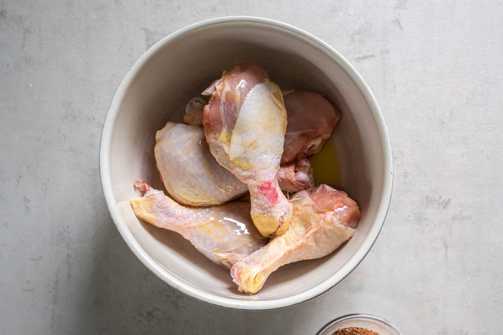 Olive oil drizzled over chicken drumsticks in a bowl.