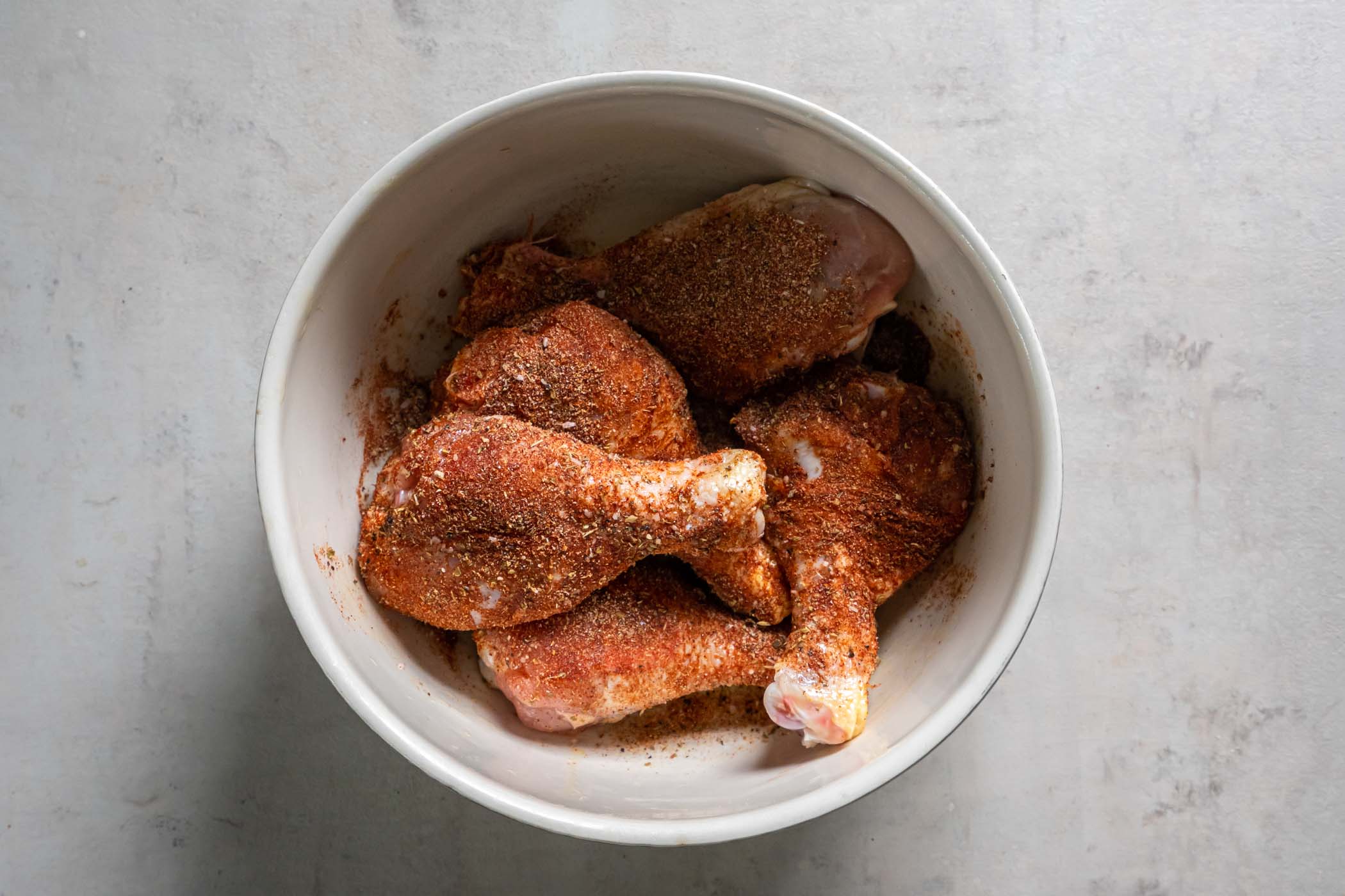 Chicken drumsticks tossed with seasonings in a bowl.