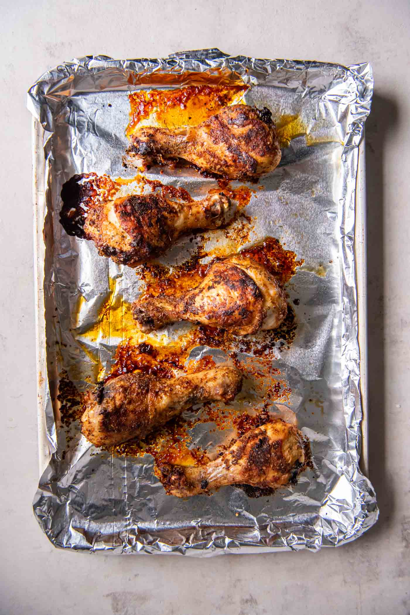 Baked chicken legs on a foil lined baking sheet.