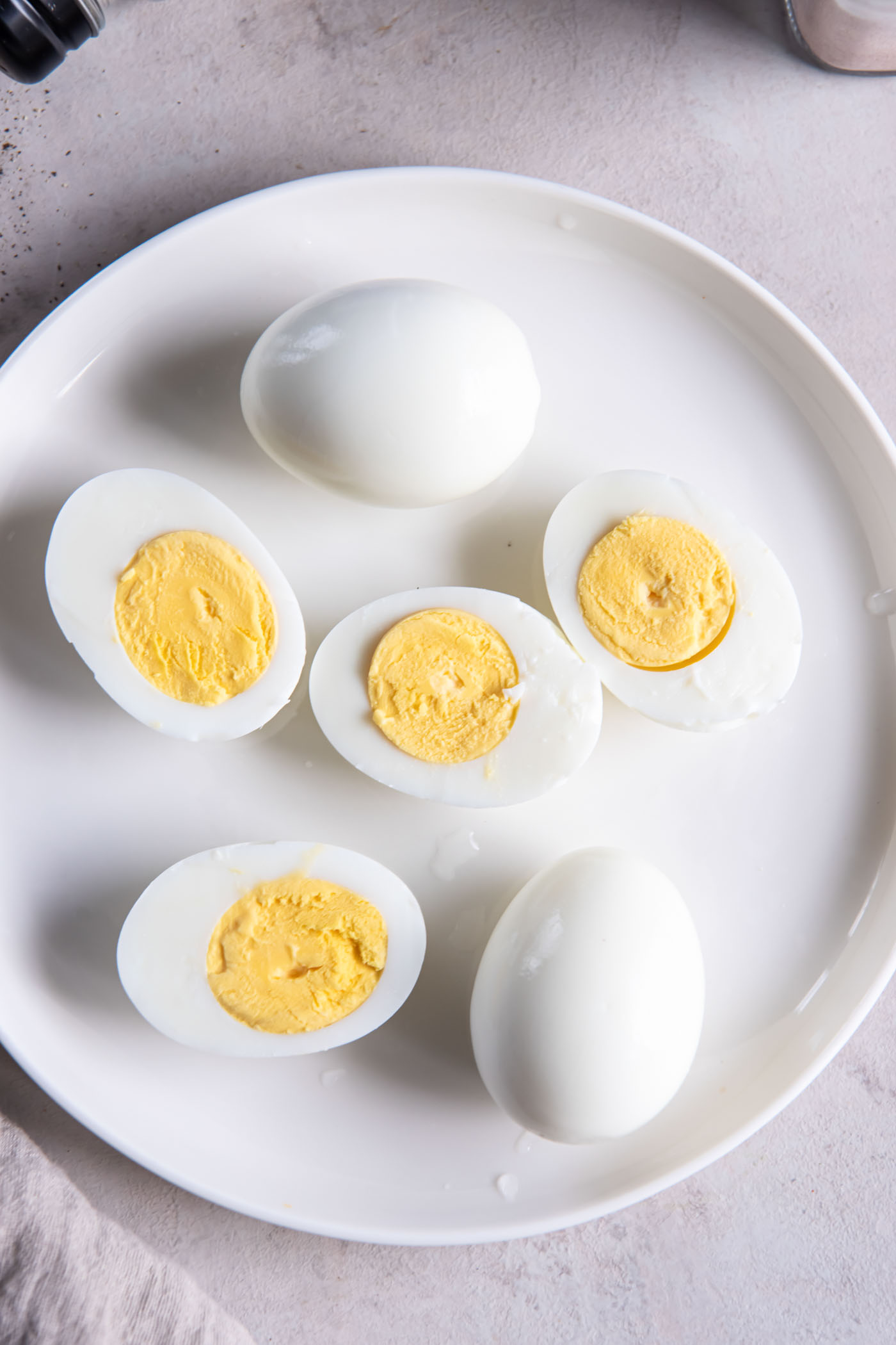 Four halved hard boiled eggs and two whole peeled eggs on a plate.