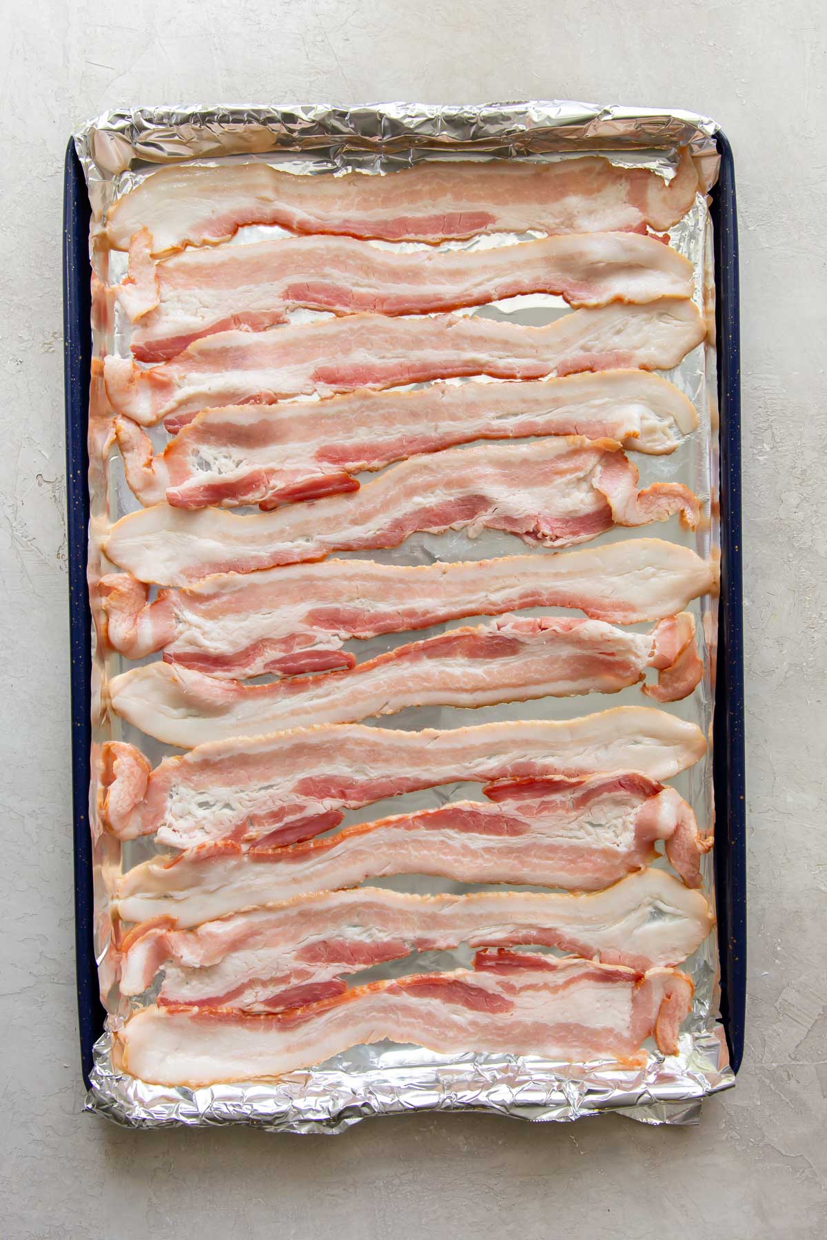 uncooked bacon on a foil-lined rimmed baking sheet