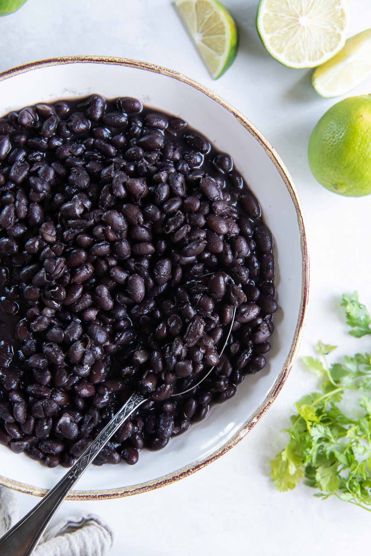 Black beans in serving bowl with spoon, with lime wedges and fresh cilantro on the side.