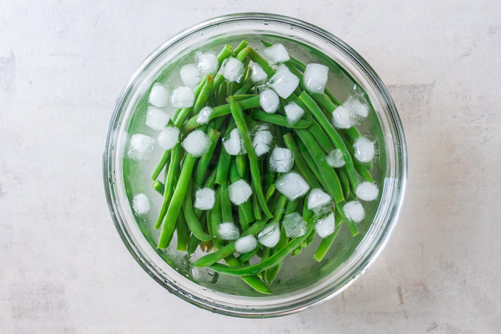 Blanched green beans in a bowl of ice water.