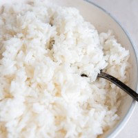 Close up of fluffy cooked white rice in a bowl with a spoon.