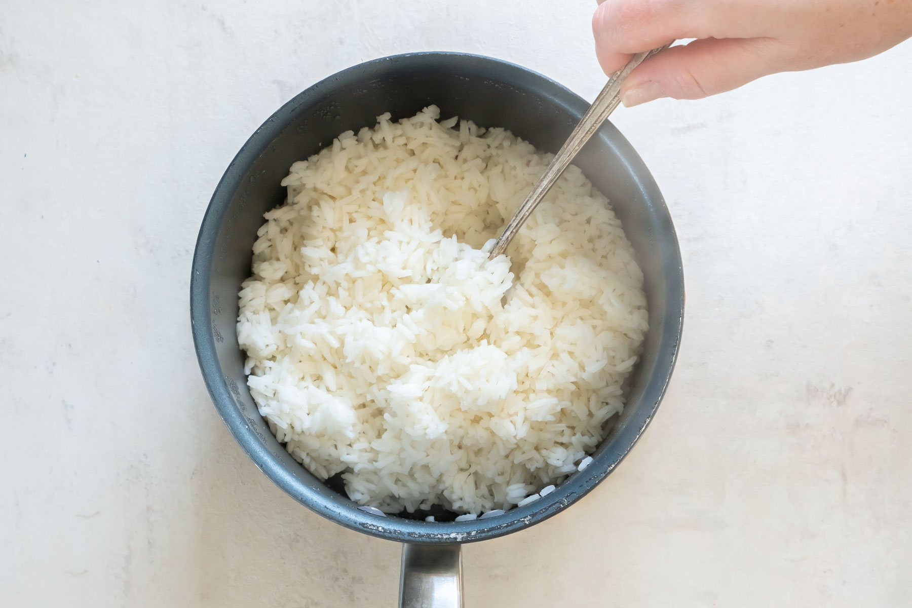 Fluffing cooked rice in pot with a spoon.