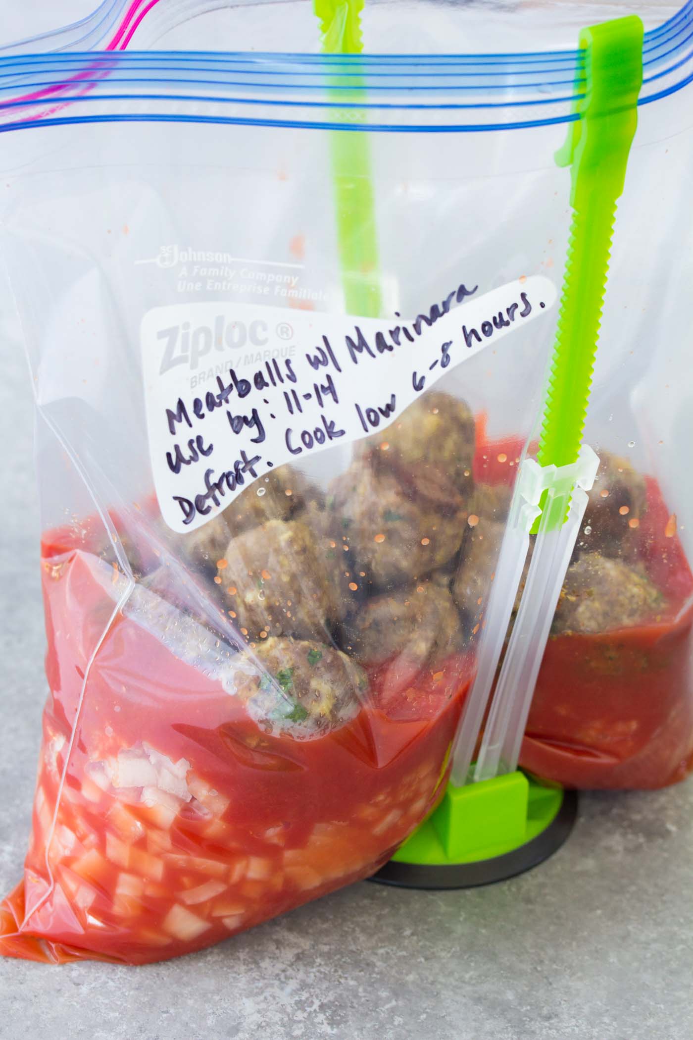 Side view of baked meatballs in zip-top bag with marinara sauce ingredients.