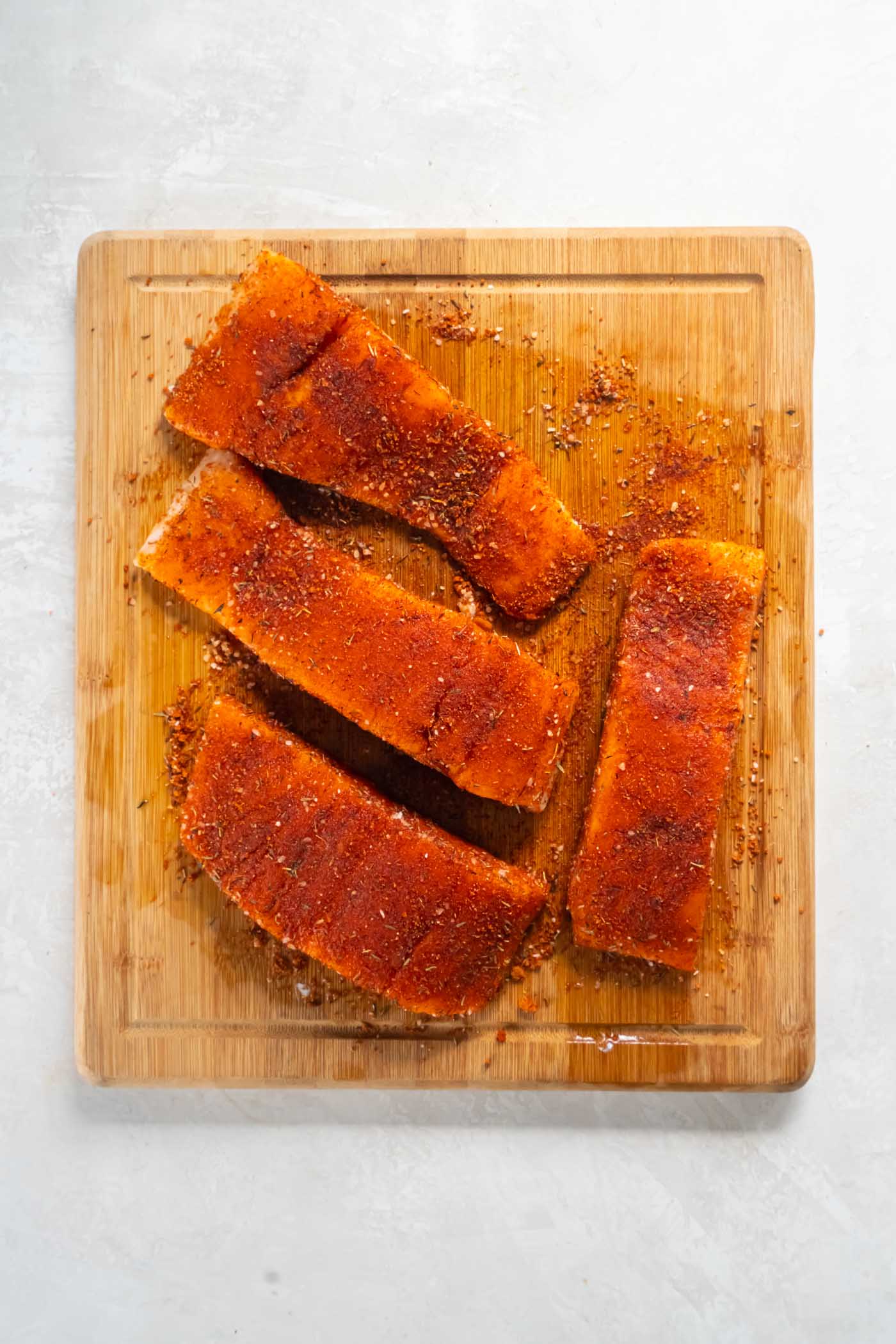 Four seasoned raw salmon fillets on a cutting board.