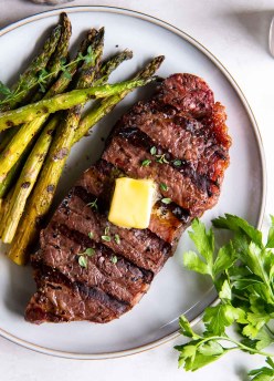Grilled steak served with a pat of butter and a side of asparagus.