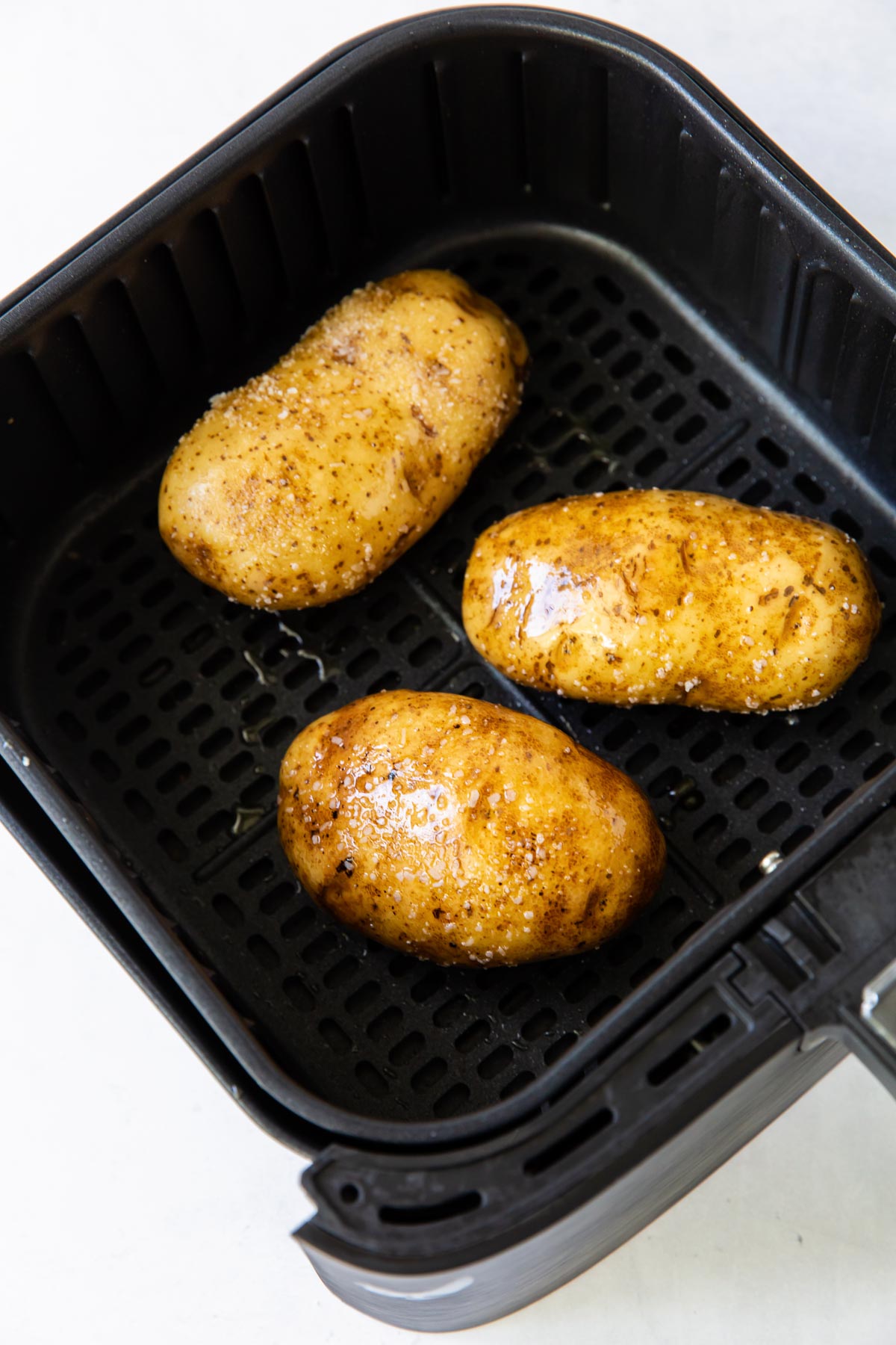 three russet potatoes rubbed with oil and salt in air fryer basket