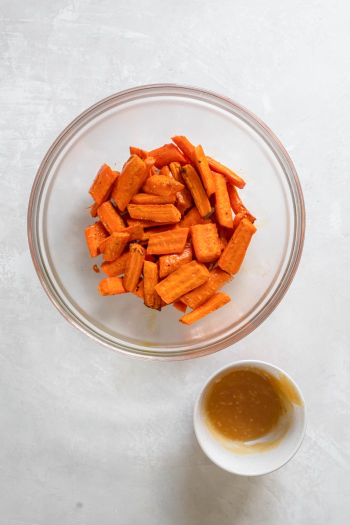 Partially cooked carrots in mixing bowl next to small bowl of honey garlic butter.