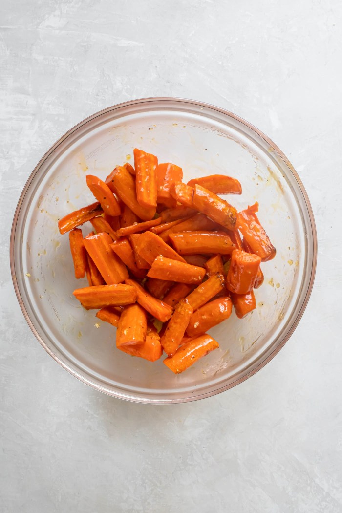Partially cooked carrots in mixing bowl tossed with honey garlic butter.