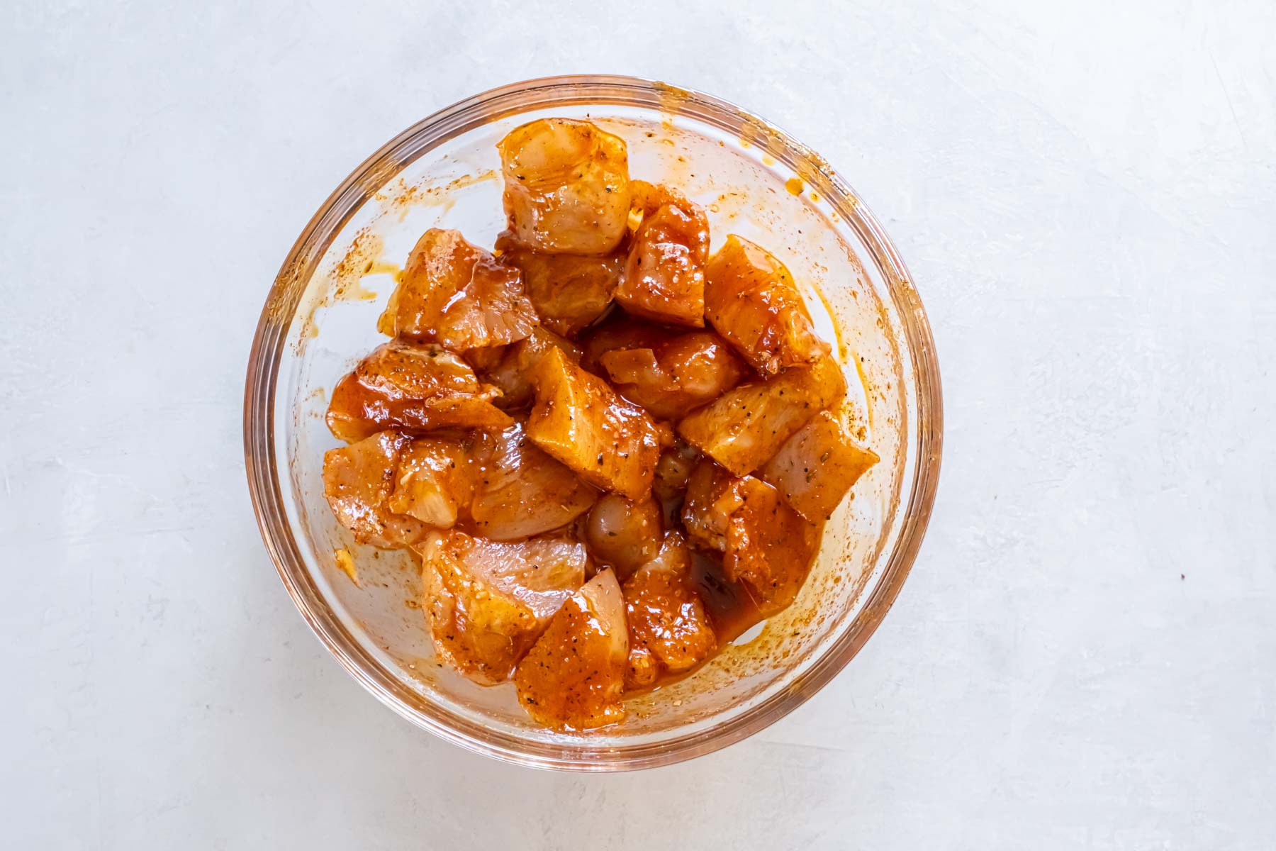 Chicken pieces in bowl coated with butter and seasonings.