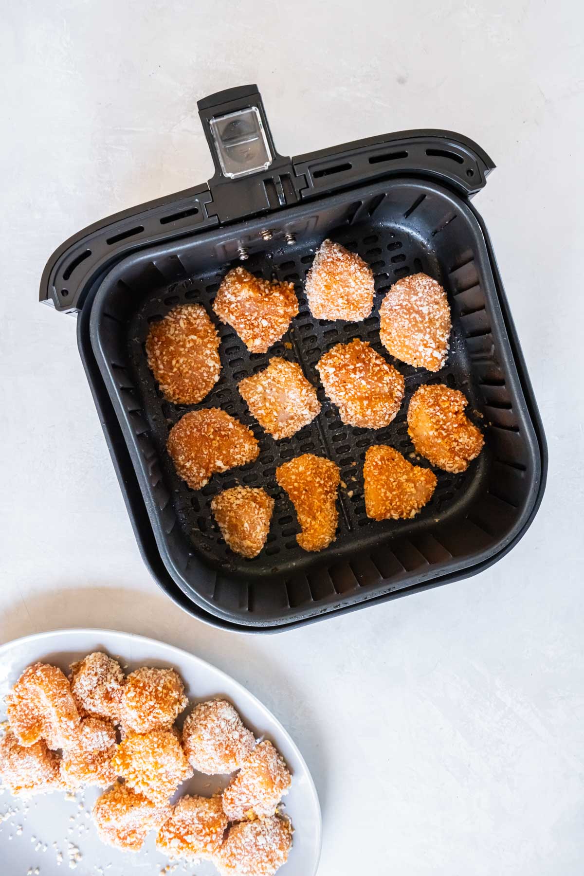 Uncooked chicken nuggets added to air fryer basket in a single layer.