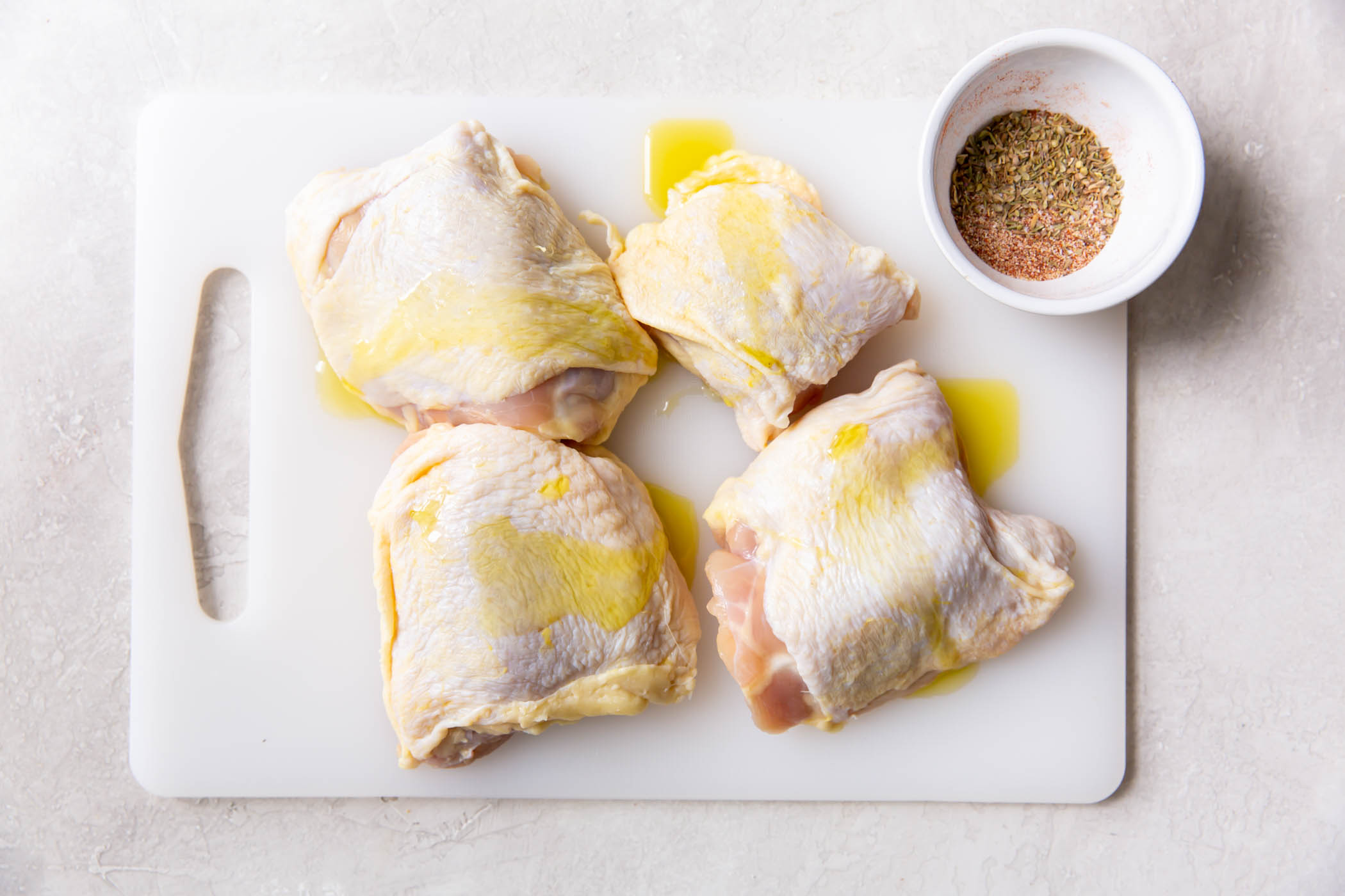Olive oil drizzled over four uncooked bone-in chicken thighs.
