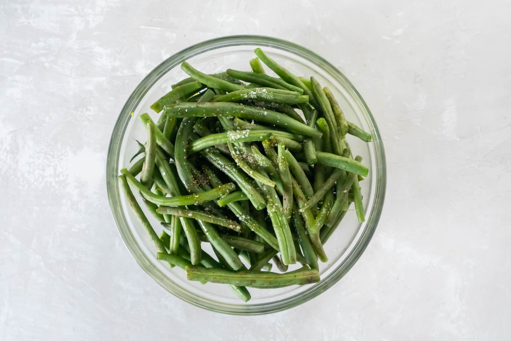 Fresh green beans in a mixing bowl with olive oil, salt and pepper.