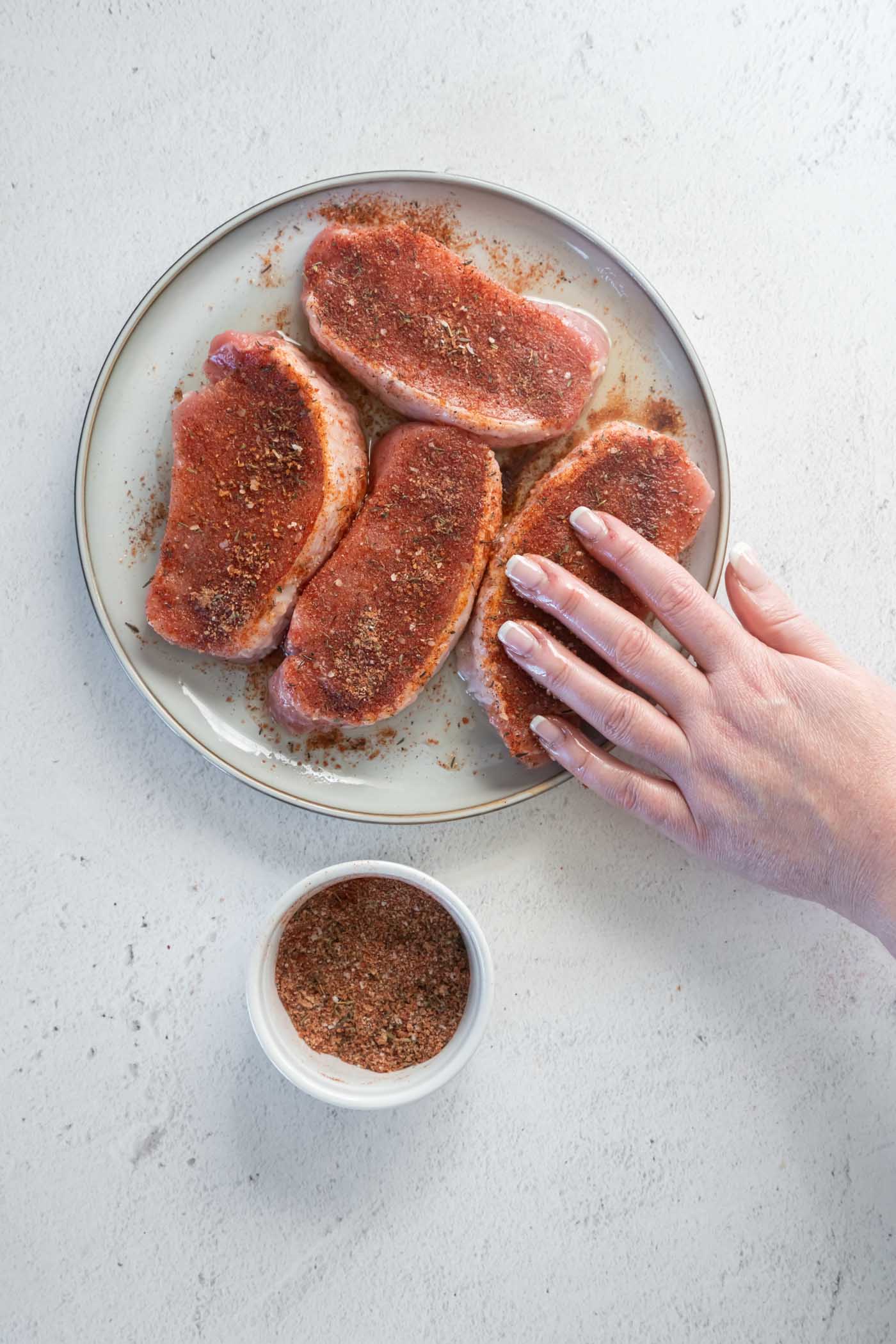 Rubbing seasonings onto four boneless pork chops.