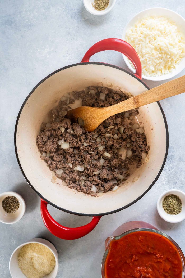 Browned ground beef, onion and garlic in pot with a wooden spoon.